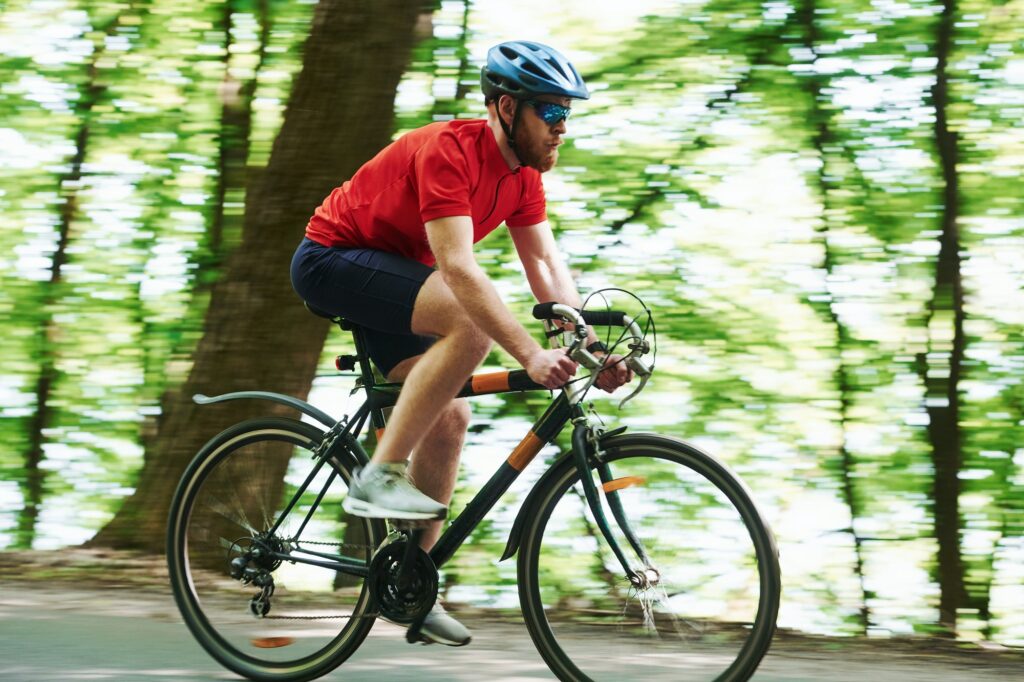 Reflection in the glasses. Cyclist on a bike is on the asphalt road in the forest at sunny day